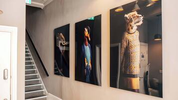 A hallway with a staircase, three framed artworks on the wall, and a door.