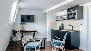 Cocina moderna con microondas, pileta y encimera de madera. Hay un comedor con dos sillas y una mesa. Un televisor de pantalla plana está montado en la pared.