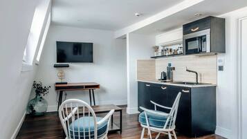 A modern kitchen with a microwave, sink, and wooden countertop. There is a dining area with two chairs and a table. A flat-screen TV is mounted on the wall.