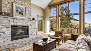A cozy living room with a stone fireplace, a large window with a view of the outdoors, and comfortable seating. - Spacious Mountain Retreat w/ Amazing Views! By Gorecreek Rentals (Avon)