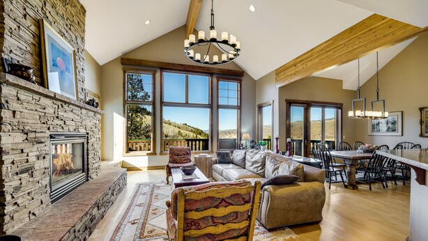 A spacious living room with a stone fireplace, large windows, a dining area, and a view of the outdoors. - Spacious Mountain Retreat w/ Amazing Views! By Gorecreek Rentals (Avon)
