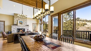 A spacious dining area with a large wooden table, chairs, and a stone fireplace. - Spacious Mountain Retreat w/ Amazing Views! By Gorecreek Rentals (Avon)