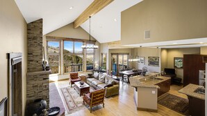A spacious living area with a stone fireplace, a large sofa, and a dining area with a kitchen island. - Spacious Mountain Retreat w/ Amazing Views! By Gorecreek Rentals (Avon)