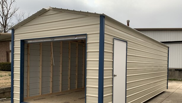 A single-story metal shed with a large open garage door, a small enclosed door, and a sloped roof. - Small house (Los cerillos)