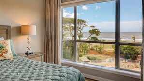 A bedroom with a large window overlooking a beach and a patio area.