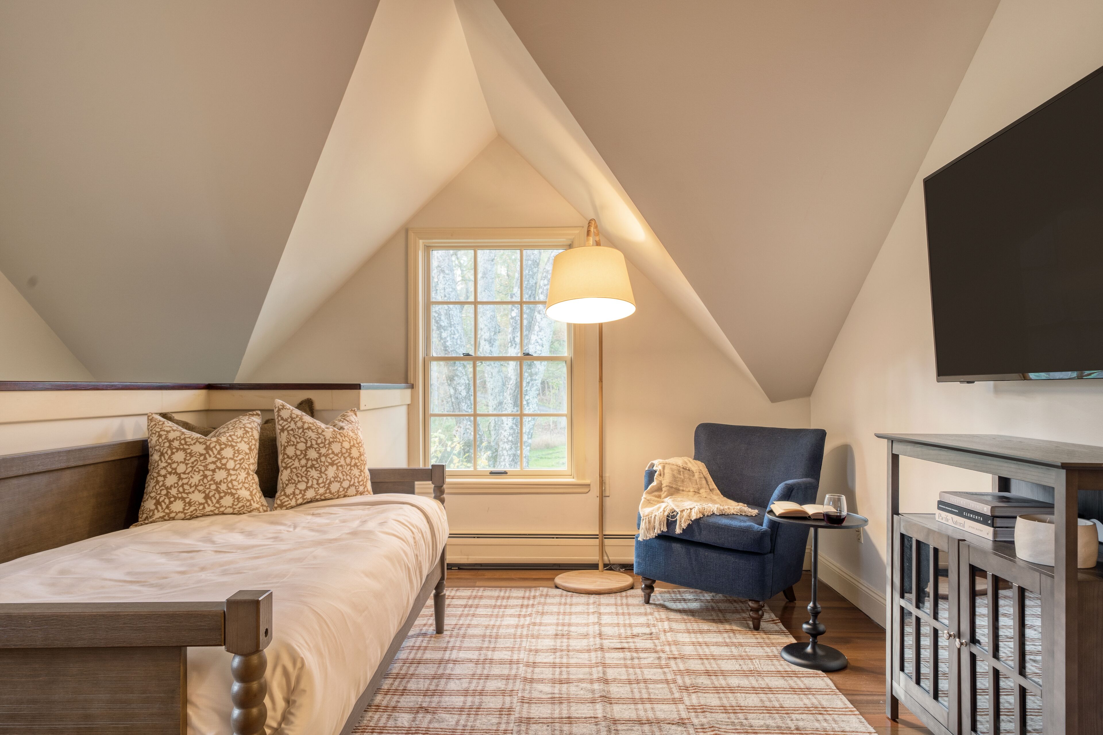 A bedroom with a bed, a chair, a table, a lamp, and a TV.