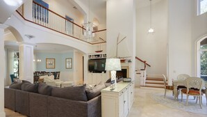 A spacious living area with a high ceiling, a built-in TV, a dining table with chairs, and a staircase leading to an upper level. - 8 bedroom/7 bathroom 3rd row corner home, luxurious and family friendly (Hilton Head Island)