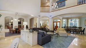 A spacious living area with a high ceiling, a dining area with wooden chairs, and a staircase leading to an upper level. - 8 bedroom/7 bathroom 3rd row corner home, luxurious and family friendly (Hilton Head Island)