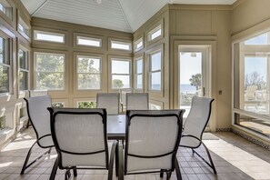 Un salón con ventanales y vista al océano, con una mesa grande y sillas.