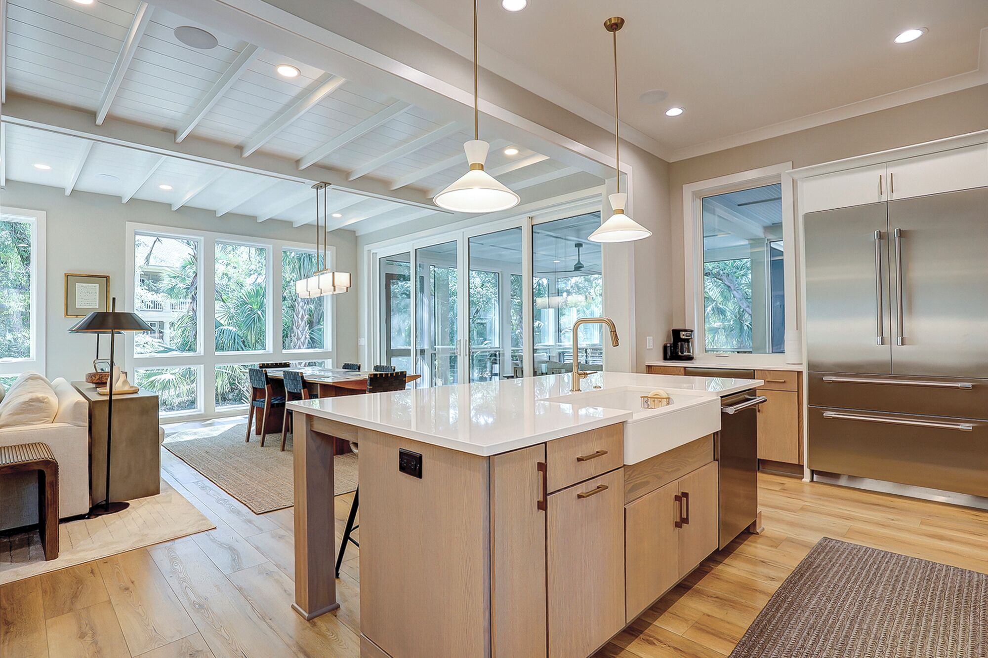 A modern kitchen with a large island, stainless steel appliances, and large windows offering views of greenery.