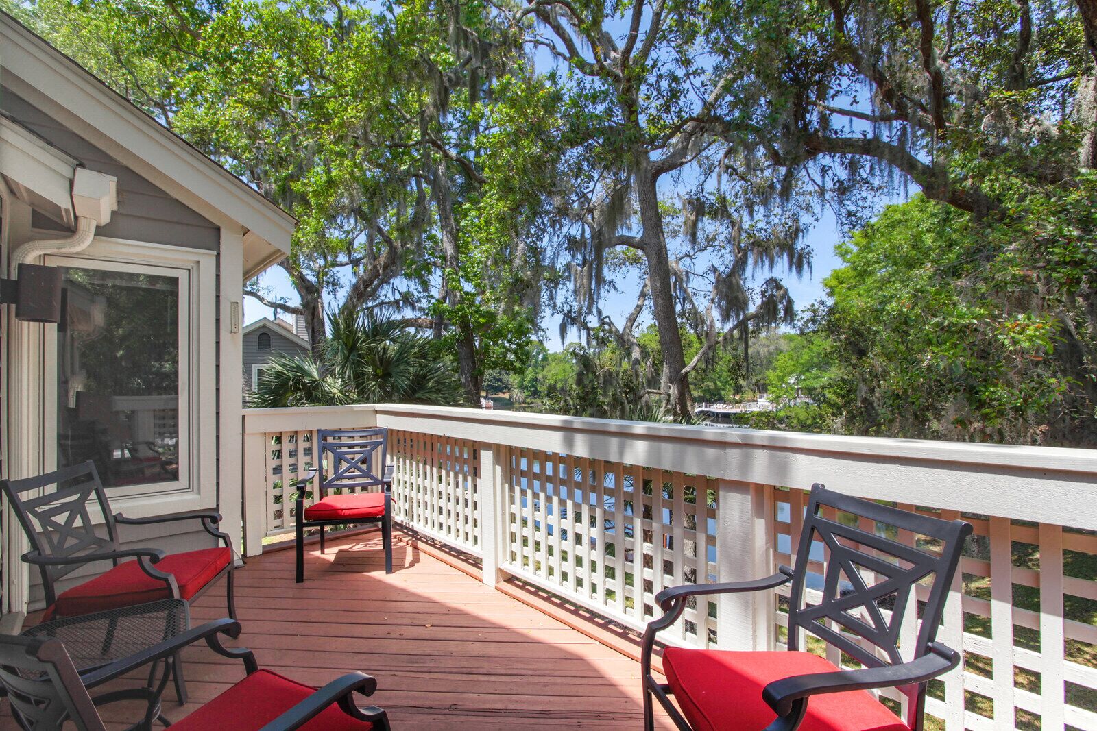 A covered deck with wooden flooring and white railings, featuring several chairs with red cushions.