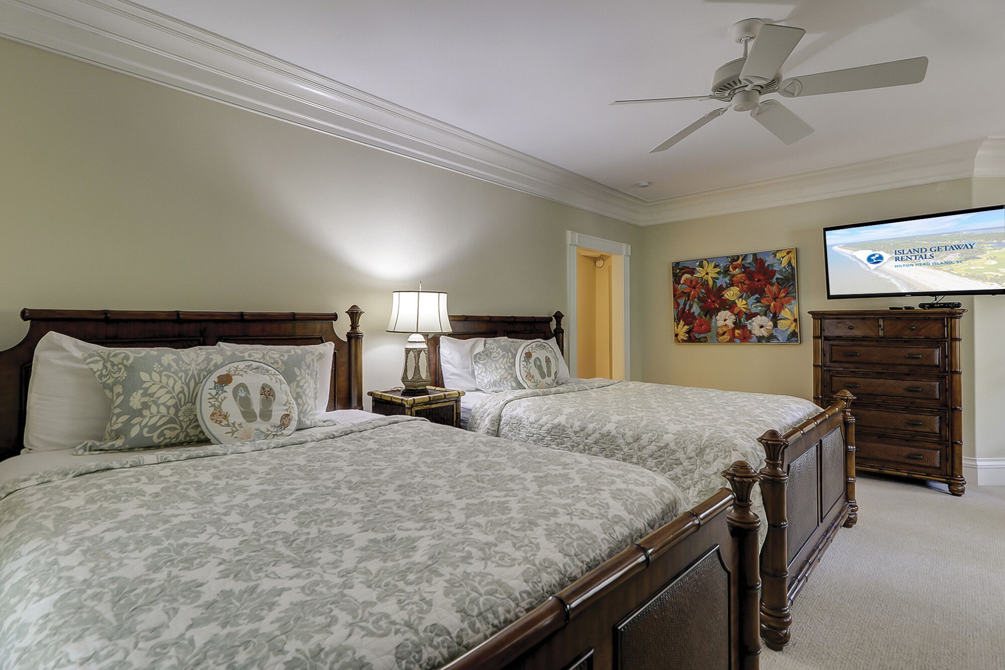 A hotel room with two beds, a ceiling fan, a TV, a dresser, and a painting on the wall.