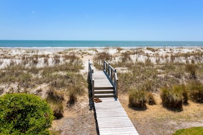 A wooden boardwalk leading to a beach with sand dunes and sparse vegetation.