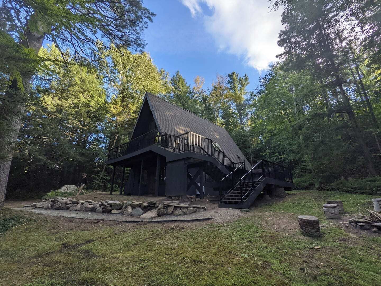 Eine Hütte mit steilem Dach, einem Balkon und einer Treppe, die darauf führt, umgeben von Bäumen.