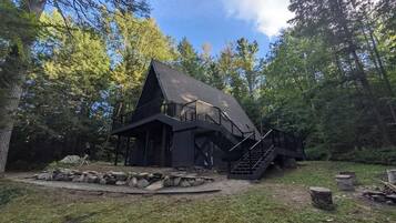 Eine Hütte mit steilem Dach, einem Balkon und einer Treppe, die darauf führt, umgeben von Bäumen.