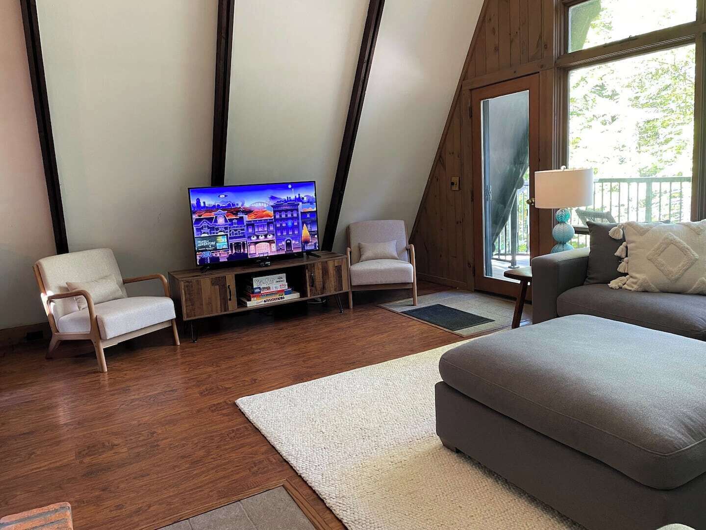 A modern living room with a television, two chairs, a sofa, and a large window.