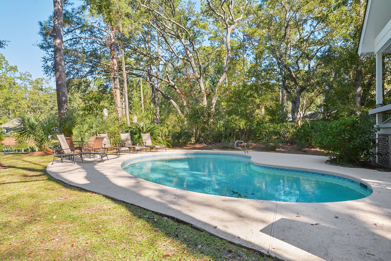 A swimming pool with a curved edge, surrounded by a concrete deck and several lounge chairs.