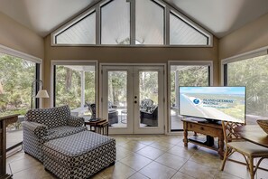 A spacious room with a high ceiling, large windows, a television, and a patterned sofa.