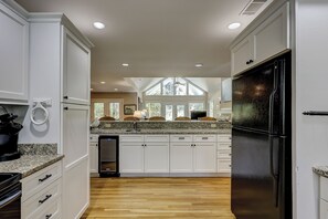 A kitchen with white cabinetry, a black refrigerator, and a wooden floor.