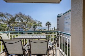 A balcony with two chairs and a table, overlooking a beach and buildings.