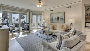 A spacious living room with a large window, a ceiling fan, a sofa, a coffee table, and a painting on the wall. - 2 bedroom villa with oceanfront views from your balcony located in Windsor Ct (Hilton Head Island)