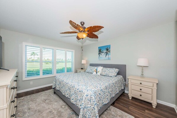 A bedroom with a bed, a nightstand, a ceiling fan, a window with blinds, and a painting on the wall.