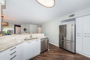 A modern kitchen with white cabinetry, a stainless steel refrigerator, and a granite countertop.