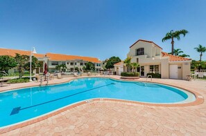 A swimming pool with a tiled deck, a building with a red-tiled roof, and a clear blue sky.
