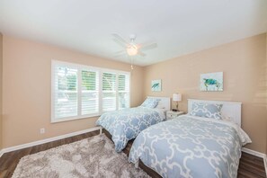 A bedroom with two beds, a ceiling fan, and artwork on the walls.