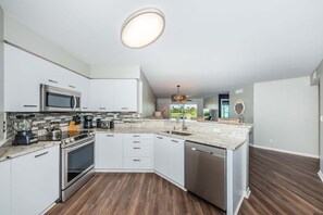 A modern kitchen with white cabinetry, a built-in microwave, a stove, and a dishwasher.