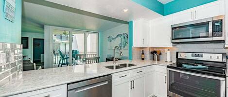A modern kitchen with white cabinets, stainless steel appliances, and a teal accent wall.