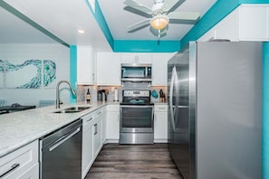 Een moderne keuken met witte kasten, roestvrijstalen apparatuur, een plafondventilator en een wand in turquoise.