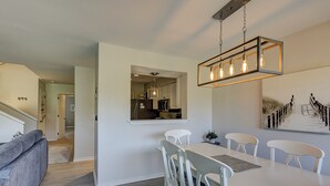 A modern kitchen with white cabinets, a dining area with a white table and chairs, and a staircase leading to another level.