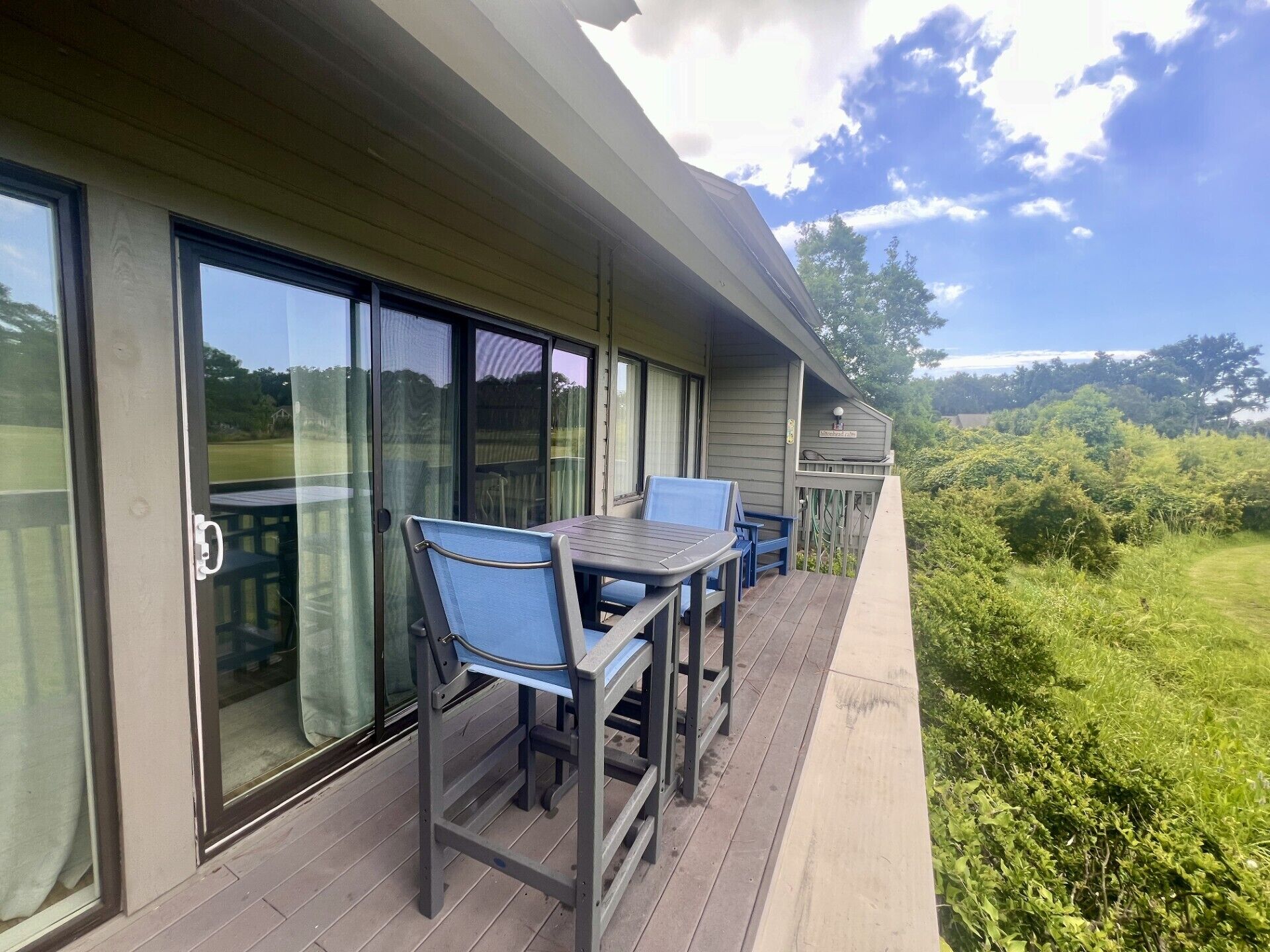 A covered outdoor area with a table and chairs, large sliding glass doors, and a view of a green landscape.
