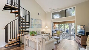 Un amplio espacio de sala con una escalera en espiral, un ventanal grande y un balcón.