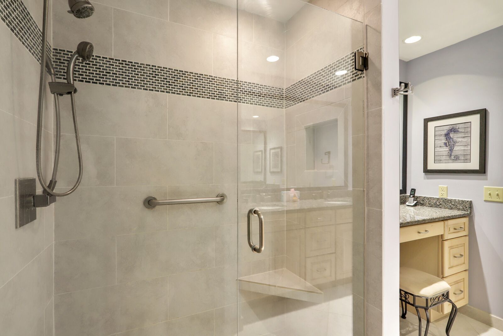 Une salle de bain moderne dotée d’une douche à parois de verre, d’un meuble-lavabo avec un plan de travail en granit et d’une œuvre d’art représentant un hippocampe, encadrée et accrochée au mur.