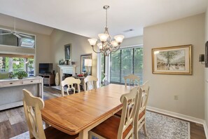A dining area with a wooden table and chairs, a chandelier, and a fireplace. - 497 Captains Cove is a lovely property located close to the beach on HHI. (Hilton Head)