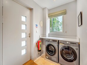A laundry room with two front-loading washing machines, a fire extinguisher, and a window with a view of trees. - Ground Floor: 
Open plan living space. (Midgham)