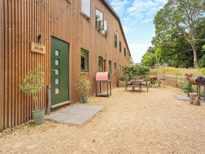 A wooden building with a green door, a barbecue grill, and a table with chairs outside. - Ground Floor: 
Open plan living space. (Midgham)