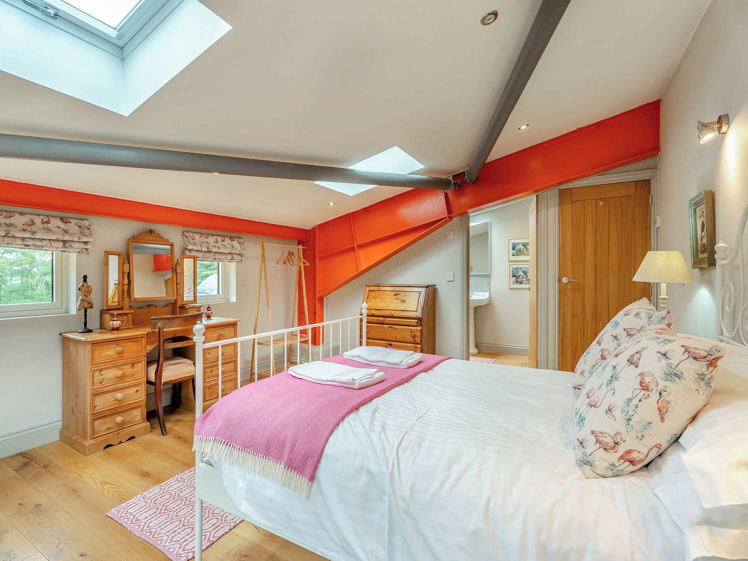 Ein Schlafzimmer mit Oberlicht, Holzmöbeln, einem Bett mit rosa Decke und einer roten Akzentwand.