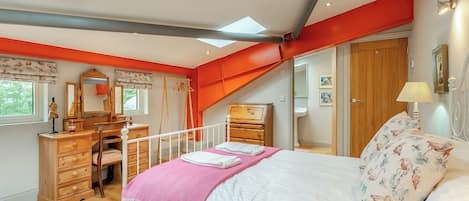 A bedroom with a skylight, wooden furniture, a bed with a pink blanket, and a red accent wall.