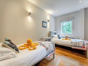 A bedroom with two beds, a window with a view of trees, and a bedside table with a lamp.