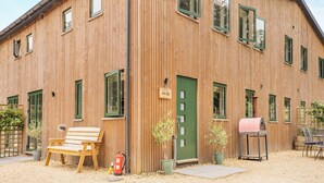 Ein Holzhaus mit mehreren Fenstern und Türen, einer Bank und einem Grill vor der Fassade.