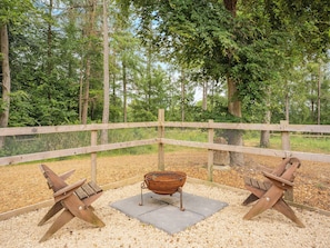 A wooden deck with a metal grill table and two wooden chairs, surrounded by a wooden fence and trees.