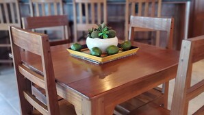 Een houten eettafel met stoelen, een kleine potplant en een schaal met limoenen.