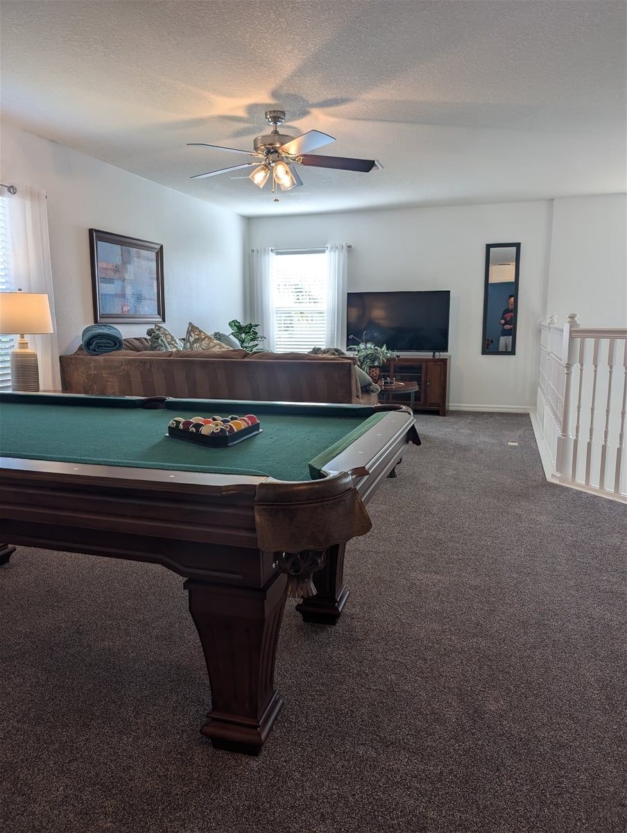 A pool table in a room with a ceiling fan, a television, and a framed picture on the wall.