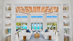 A spacious living area with white furniture, a wooden coffee table, and a view of the ocean. - Ba Roos Beach House/Iconic Tar Bay Estate with 300’ of Direct Beachfront (Mosstown)
