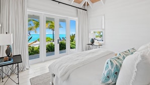A bedroom with a large bed, white curtains, a desk with a laptop, and a view of the ocean. - Ba Roos Beach House/Iconic Tar Bay Estate with 300’ of Direct Beachfront (Mosstown)