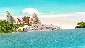 A beach with a clear blue pool, a white umbrella, and a wooden chair. - Ba Roos Beach House/Iconic Tar Bay Estate with 300’ of Direct Beachfront (Mosstown)