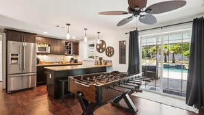 Cozinha moderna com uma ilha grande, eletrodomésticos de aço inoxidável e área de piscina com mesa de pebolim.